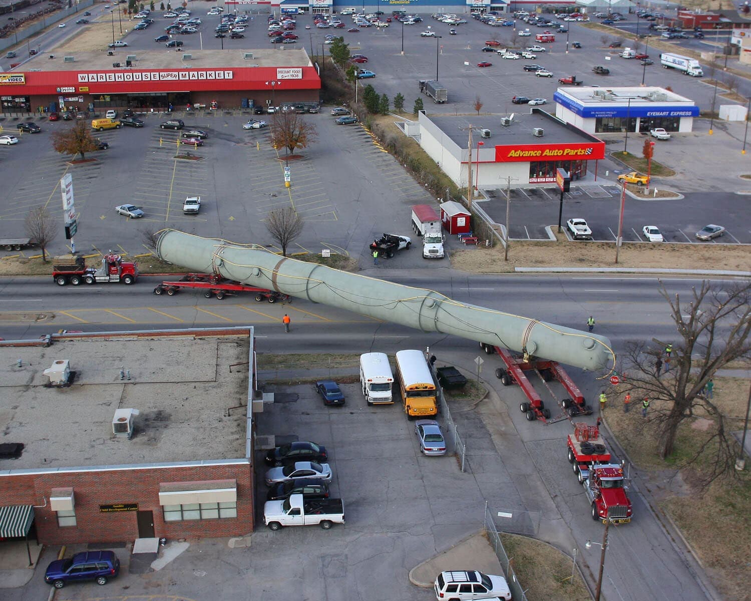 Aerial view of a long vessel on an Emmert transporter moving through a commercial intersection with escort vehicles